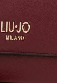 Burgundy leather wallet featuring gold-tone "LIU·JO MILANO" logo, textured surface, and stitched accents along the edges.