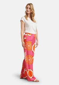 Fließende, rosa gemusterte Hosen mit orangefarbenen Obstmotiven; elastischer Bund. Kombiniert mit einem weißen, kurzärmeligen Oberteil und leichten Sandalen.