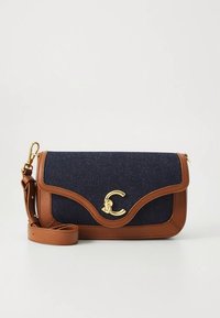 Blue denim crossbody bag with brown leather accents, gold hardware, and a curved flap design. Features a detachable strap for versatility.
