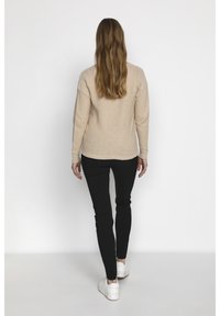 Beige tröja med långa ärmar, rundad hals och ribbat fåll, i kombination med svarta slim-fit byxor. Skorna är vita sneakers med tjock sula.