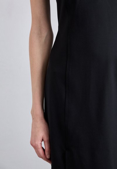 Black dress with a smooth texture. A close-up of a slender arm holding the fabric, showcasing clean lines and fitted design details.