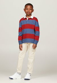 Polo a maniche lunghe a righe blu e rosse con colletto bianco, abbinato a pantaloni cargo beige e sneakers bianche.