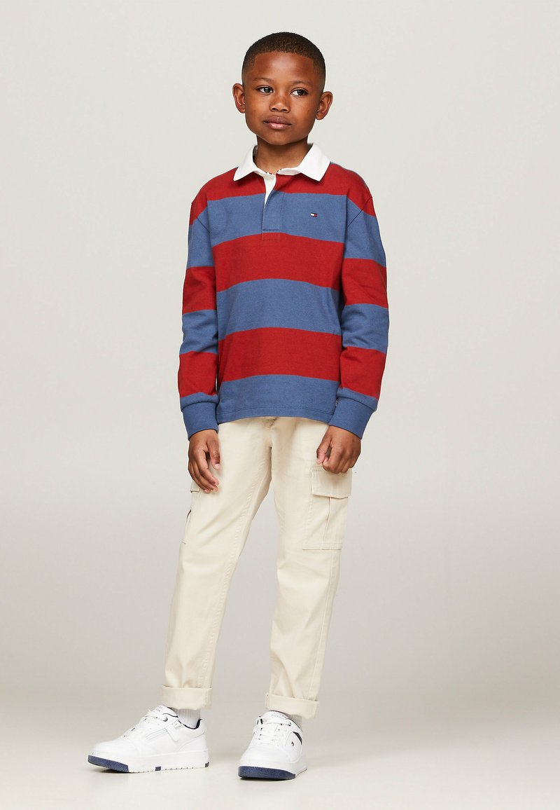 Polo a maniche lunghe a righe blu e rosse con colletto bianco, abbinato a pantaloni cargo beige e sneakers bianche.