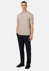 Svetlo bež majica s kratkimi rokavi, izdelana iz mehkega materiala, v kombinaciji s temno navy hlačami in črnimi supergami. Preprost dizajn, brez vidnih vzorcev.