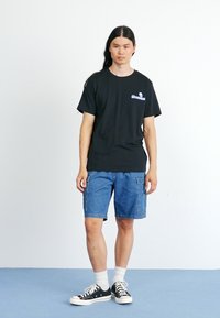 Sort bomulds t-shirt med grafisk logo, parret med blå denim cargo shorts. Outfit fuldendes med sorte sneakers og hvide ankelstrømper.