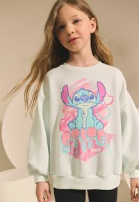 Lys mintgrøn oversized sweatshirt med et farverigt grafik af Stitch, med teksten "STITCH" og "OHANA" i fed, legesyg skrifttype.
