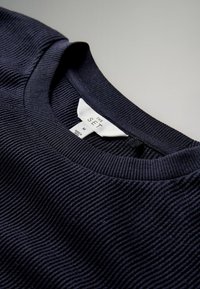 Mørkeblå ribstrikket sweater med rund halsudskæring, med en mærkat hvor der står "THE SET" og størrelse "M," lavet af tekstureret stof.