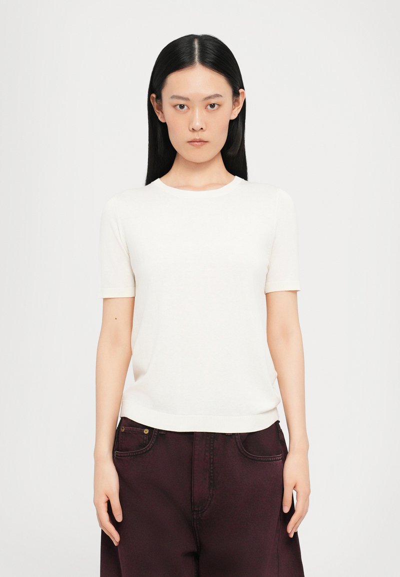 T-shirt bianco a maniche corte con scollo rotondo, texture liscia e design aderente, abbinato a pantaloni bordeaux scuri.