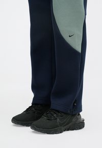 Nike φόρμες σε ναυτικό μπλε με ανοιχτό πράσινες λεπτομέρειες και χωρίς ραφές, συνδυασμένες με μαύρα υφασμάτινα αθλητικά παπούτσια με καουτσούκ σόλα.