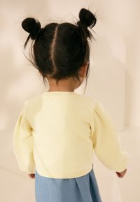 Lysegul sweatshirt med puffede ærmer, kombineret med en lyseblå nederdel. Teksturen fremstår blød med rund halsudskæring og en rynket kant.