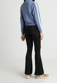 Giacca azzurra chiara con strisce blu navy sulle maniche, abbinata a pantaloni neri a zampa. Il modello indossa sneaker beige e rosa.