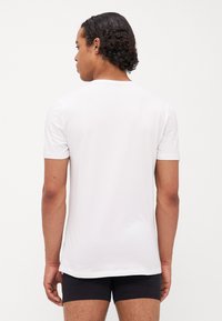 Weißes T-Shirt mit kurzen Ärmeln aus glattem Stoff, mit Rundhalsausschnitt und lässiger Passform, von hinten auf einem Modell präsentiert.