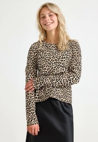 Top de manga larga en tela beige con un estampado de leopardo negro. Cuenta con cuello redondo y un ajuste relajado con un dobladillo ligeramente curvado.