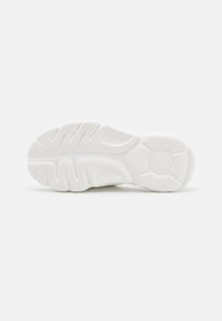 Suela de zapatilla blanca con una superficie de goma texturizada; presenta un patrón de ondas, un logotipo redondo y un diseño contorneado para agarre y comodidad.