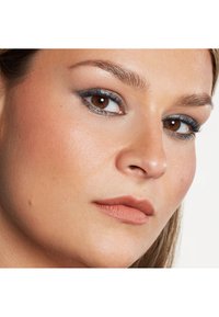 Närbild av ett ansikte med ljus, jämn hud; bruna ögon med grå ögonskugga; definierade ögonbryn; och matt, naken läppfärg.