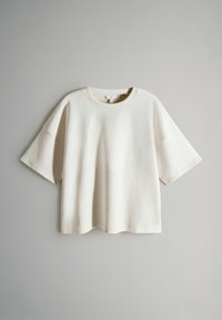 Kurzes, cremefarbenes T-Shirt aus einem weichen, strukturierten Stoff mit rundem Halsausschnitt und lockerer Passform. Der Saum ist leicht abgerundet.