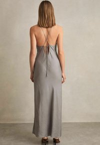 Abito maxi in satin argento con schiena bassa, caratterizzato da spalline incrociate e un accento annodato. Texture liscia e design fino al pavimento.