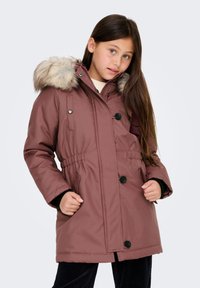 Rózsaszín parka kabát bolyhos béléssel ellátott kapucnival, gombos és rugós derékpántos részletekkel, valamint két oldalsó zsebbel. Jellemzője a sima, texturált anyag.