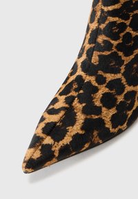 Leopardmönstrad sko med spetsig tå i svart och tan, med en mjuk textur, distinkta djurmönster och en elegant, avlång form.