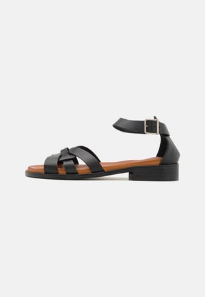 Black leather sandal with multiple straps, a buckled ankle strap, and a brown leather footbed. Features a low block heel.