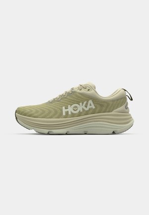 Zapatilla deportiva de color verde claro con parte superior de malla texturizada, logo de HOKA, cuello acolchado y entresuela gruesa para amortiguación. Suela de goma con patrón de tracción.