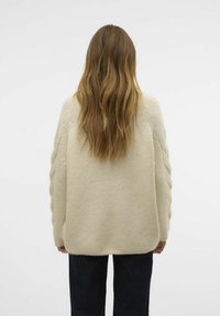 Cremfarbener Strickpullover mit lockerer Passform, der strukturierte Zopfmuster-Details an den Ärmeln aufweist. Weiches, flauschiges Material.