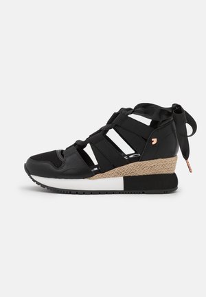 Baskets à talon compensé noires avec semelle intermédiaire tissée, brides latérales ouvertes, bout en mesh et fermeture par ruban au talon sur fond blanc.
