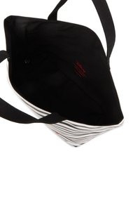 Sac fourre-tout à rayures noir et blanc avec des poignées noires robustes, dotée d'un intérieur noir et d'une étiquette de logo rouge. Conception spacieuse pour un usage polyvalent.