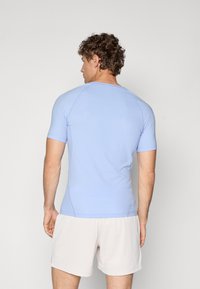 Lyseblå sportsjakke med korte ermer, med en glatt tekstur og mesh-detaljer på sidene, iført lette shorts.