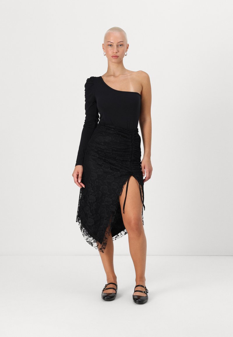 Μαύρο κορμάκι με έναν ώμο και ρυάκια μακρύ μανίκι, συνδυασμένο με μια μαύρη δαντελένια φούστα με ψηλή σχισμή και λεπτομέρεια με κορδόνι. Flat μαύρα παπούτσια.