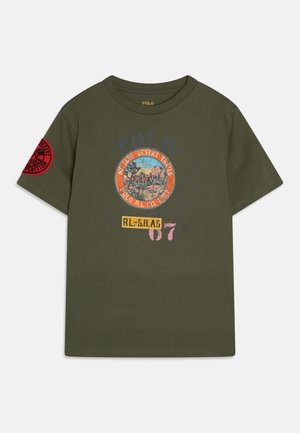 Oliwkowa koszulka z krótkim rękawem i okrągłym dekoltem, z grafiką o tematyce pustynnej i napisem "Mojave Desert Trails" oraz czerwoną naszywką "Desert Expedition" na rękawie.