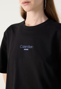 Black cotton t-shirt with a crew neckline. Features a blue embroidered logo reading "Calvin Klein JEANS" on the chest.