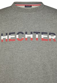 Grijze trui met ronde hals met "HECHTER" in vetgedrukte, multi-kleurige letters (marineblauw, wit, rood) over de voorkant. Zachte textuur.