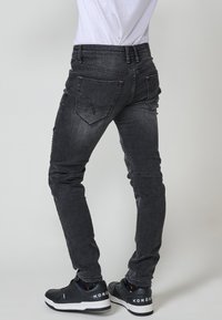 Sötétszürke farmernadrág, slim fit fazonnal, öt zsebbel és diszkrét kopással. Fekete sportcipővel viselve.