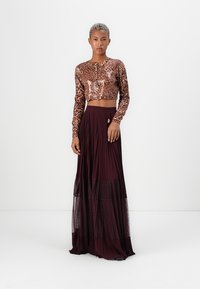 Top a maniche lunghe in stampa leopardata, accorciato, abbinato a una gonna plissettata fluente di colore bordeaux con una sovrapposizione trasparente a pois.