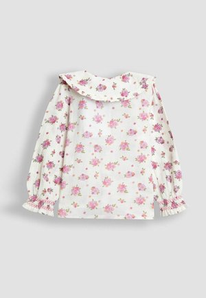 Cvečni bluzon z belim ozadjem, okrašen z rožnatimi in zelenimi cvetličnimi vzorci, z nabrano ovratnico in elastičnimi napihnjenimi rokavi.