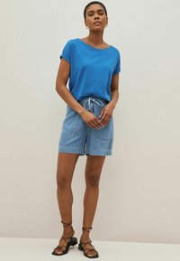 Blå bomulls t-shirt med uppvikta ärmar, tillsammans med ljusa denimshorts med dragsko i midjan och två framfickor. svarta sandaletter med remmar.