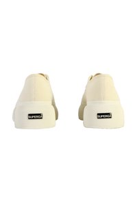 Sneaker in tela beige con suola in gomma testurizzata, dotate di un logo Superga nero sul tallone. Design semplice con punta arrotondata e profilo basso.