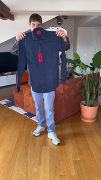 Camisa botão azul-marinho com gola, apresentando uma textura suave e uma etiqueta de marca vermelha. A camisa tem mangas longas e um corte casual.