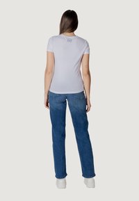 T-shirt bianco a maniche corte con un logo sulla schiena, abbinato a jeans in denim azzurri a vita alta e sneaker bianche.