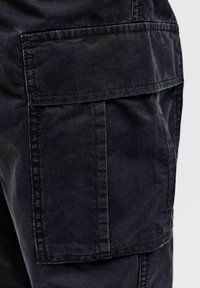 Schwarze Stoff-Cargohosen-Tasche mit Klappe, sichtbaren Nähten und verstärkten Nähten an der Beinseite.