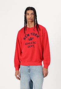 Sudadera roja de algodón con cuello redondo, mangas largas y la frase "NEW YORK GAP ATHLETIC DEPT." impresa en azul marino.