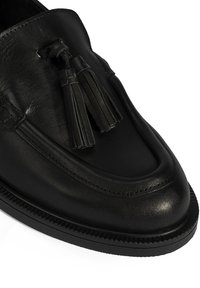 Schwarze Lederloafer mit Quastenakzenten, abgerundeter Spitze und strukturiertem Sohlenprofil. Mit glatter Oberfläche und genähten Details entlang des Obermaterials.