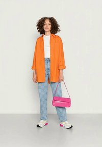 Camisa laranja de botões, t-shirt branca, jeans xadrez azul claro, mala rosa e sapatilhas brancas com detalhes rosas.