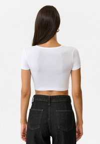 Witte, cropped t-shirt met korte mouwen, met een ronde halslijn en een gladde textuur, gecombineerd met hoge taille, donkere spijkerbroek.