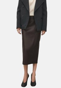 Falda de cuero marrón, hasta la rodilla, con una textura suave. Combinada con un abrigo gris de doble botonadura y tacones negros.