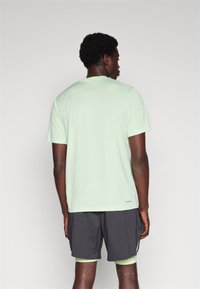 Helles grünes Sport-T-Shirt aus glattem Stoff, mit kurzen Ärmeln, Rundhalsausschnitt und einem dezenten Markenlogo am Saum.