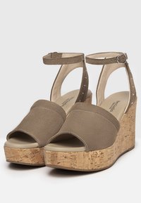 Beige Sandalen mit offenem Zehenbereich und Keilabsatz, Korkplattform, oberer Teil aus weichem Wildleder, Knöchellasche mit verstellbarem Schnallenverschluss und dezenten Nietenakzenten.