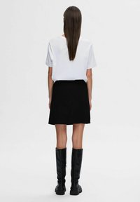 T-shirt bianco a maniche corte, mini gonna nera e stivali neri al ginocchio. Tessuto liscio con una vestibilità rilassata e un design minimalista.