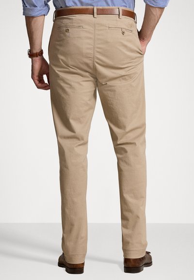 Béžové bavlnené nohavice so širokým strihom, s dvoma zadnými vreckami a hnedým koženým opaskom, zobrazené zozadu.